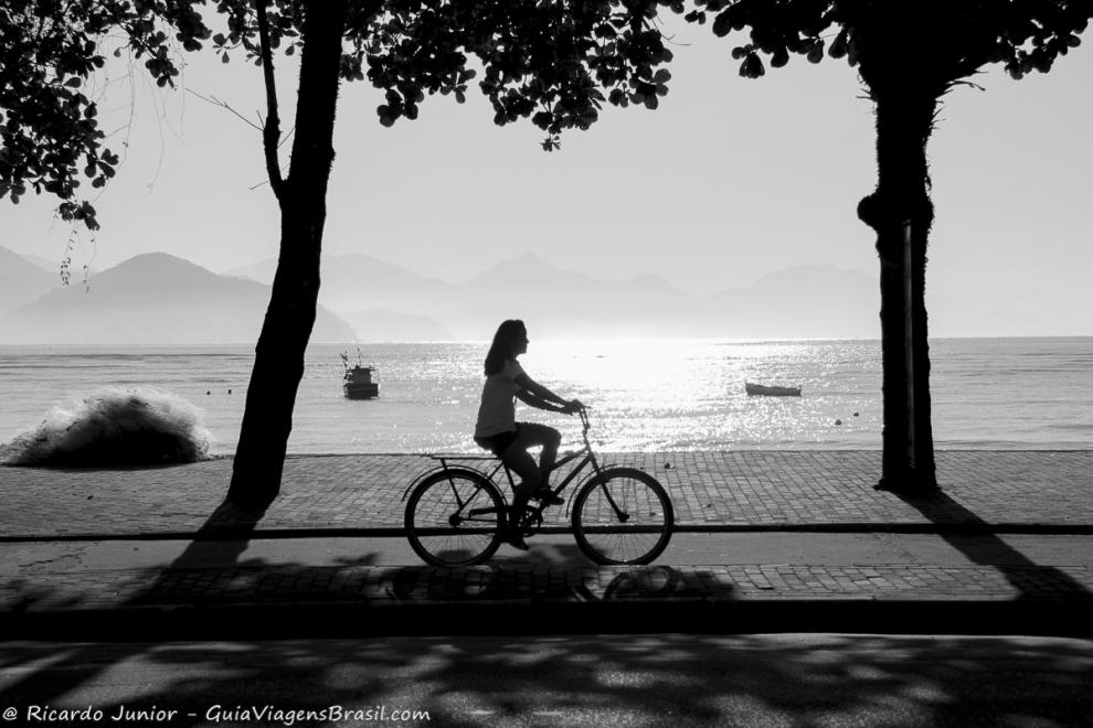 Imagem preto e branco de uma menina andando de bicicleta na orla da Praia do Itaguá.